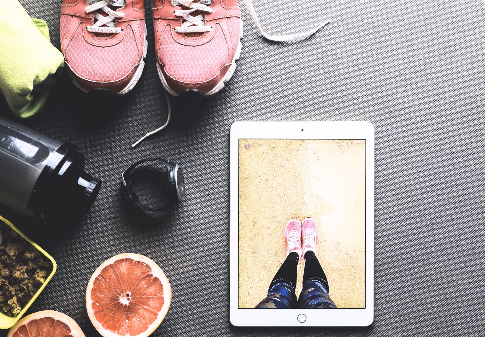 Fitness items, including shoes, a smartwatch, a water bottle, and a tablet showing a close-up of shoes on a sandy surface.