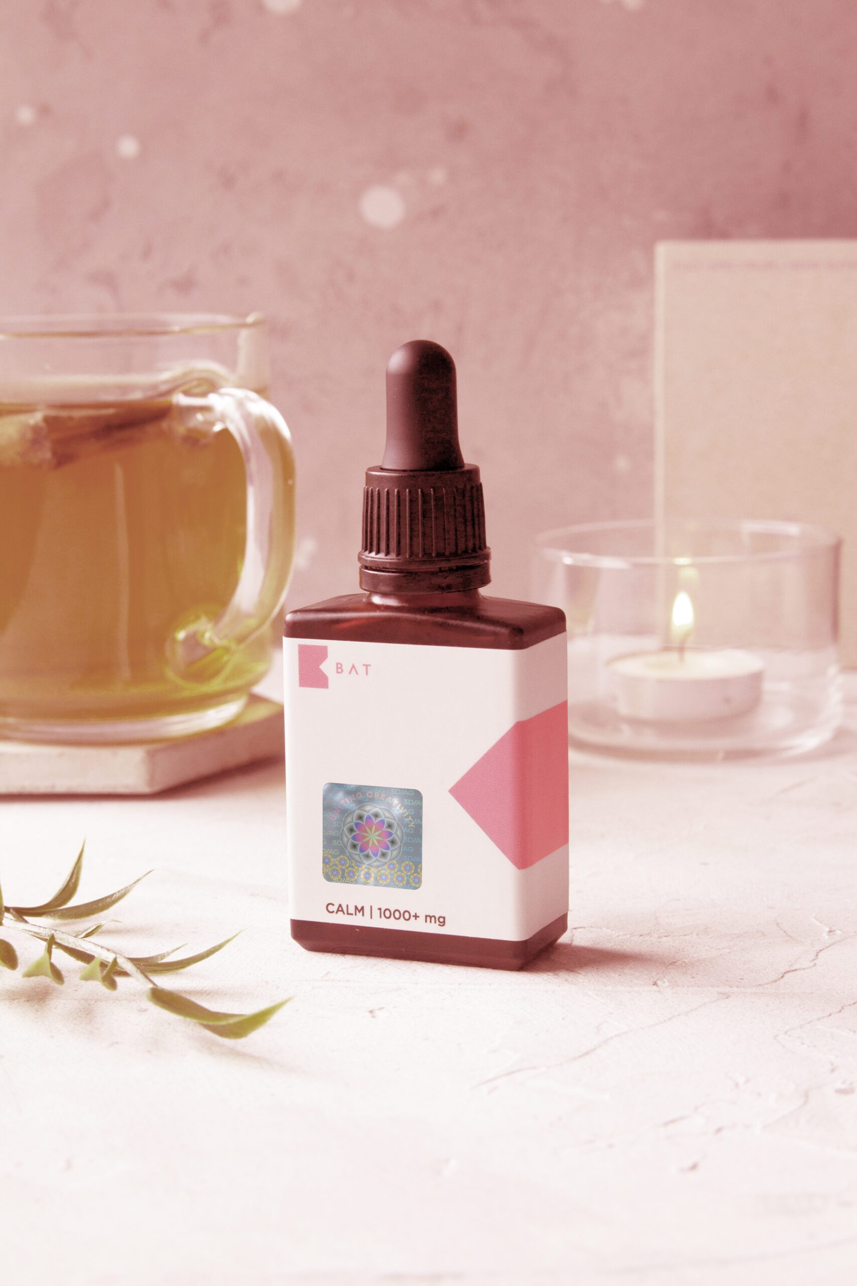 Calm oil dropper bottle labeled 'Calm 1000+ mg' featuring a holographic security label, with a tea cup and candle in the background.