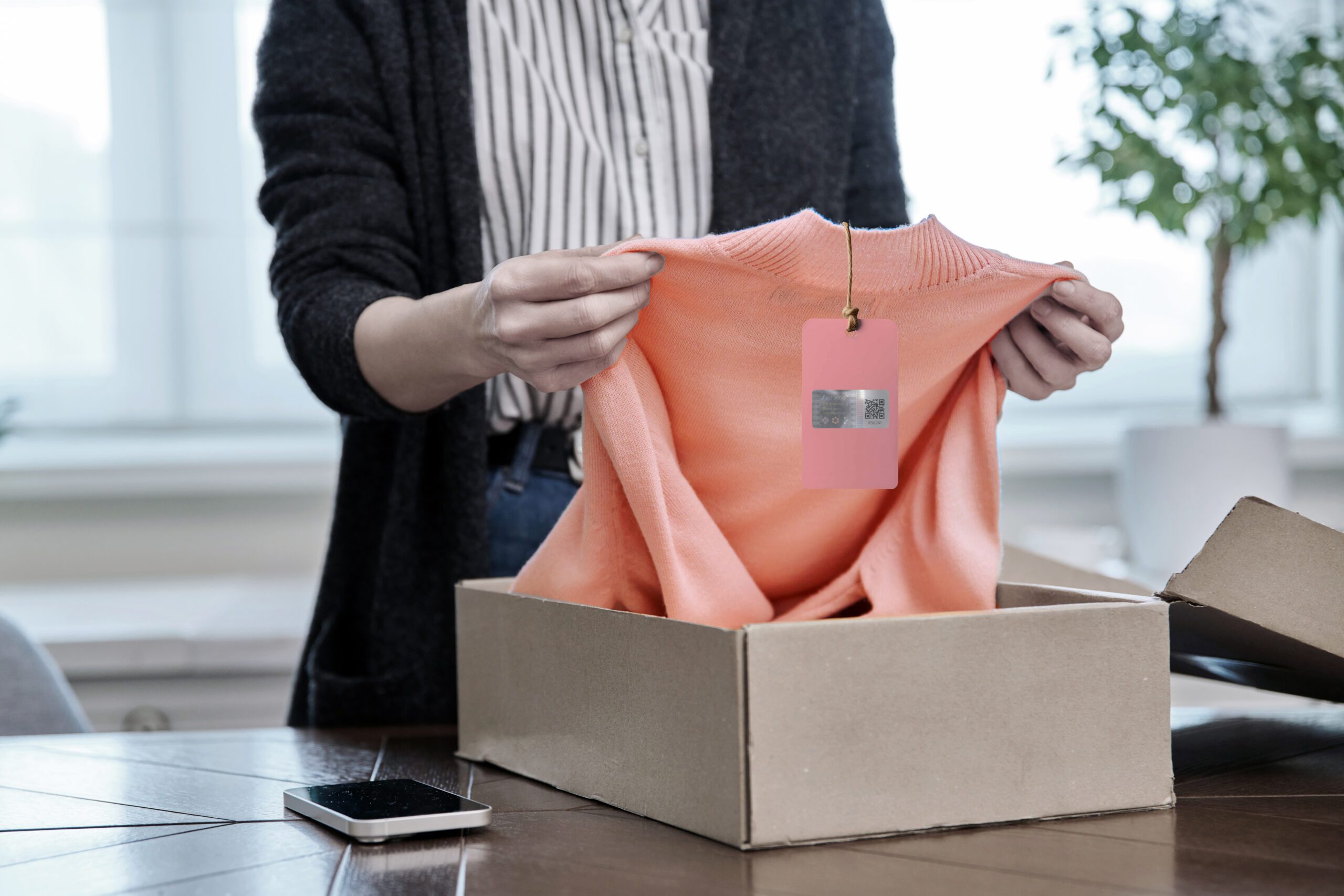 Person holding a pullover with a holographic security label and QR code, used for product authentication and preventing counterfeiting in the fashion industry.